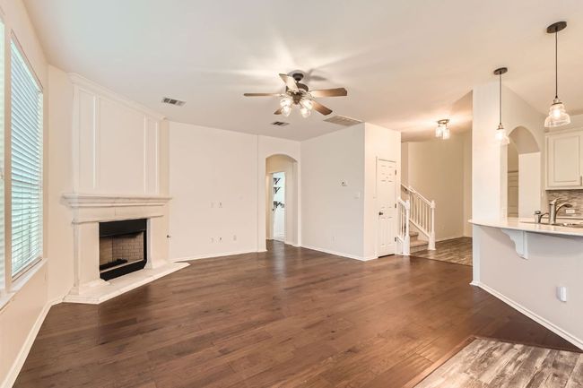 Unfurnished living room featuring arched walkways, a ceiling fan, stairs, dark wood-type flooring, and a fireplace with raised hearth | Image 11