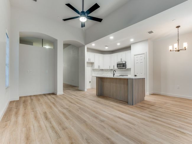 Kitchen with arched walkways, light wood-type flooring, white cabinets, ceiling fan, and a chandelier | Image 9
