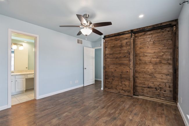 primary bedroom with a barn door, wood finished floors, visible vents, and baseboards | Image 18