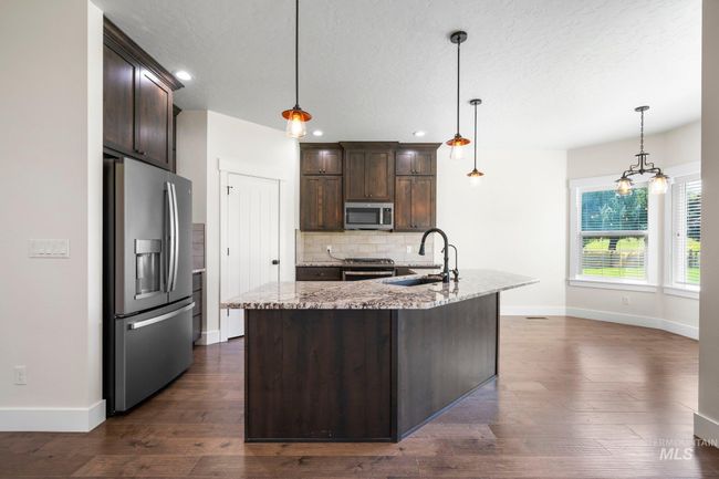 Kitchen with appliances with stainless steel finishes, dark brown cabinetry, decorative backsplash, dark wood-style flooring, and a textured ceiling | Image 5