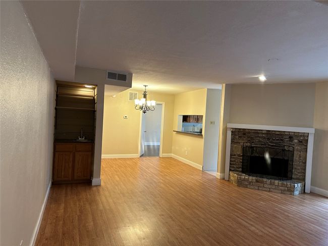Unfurnished living room featuring wood finished floors, a chandelier, and a fireplace with raised hearth | Image 7
