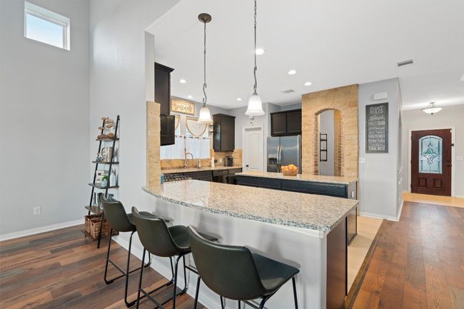 Kitchen with stainless steel fridge, tasteful backsplash, wood finished floors, light stone counters, and a peninsula | Image 11