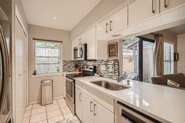 Kitchen featuring stainless steel appliances, white cabinetry, tasteful backsplash, light tile patterned floors, and healthy amount of natural light | Image 4