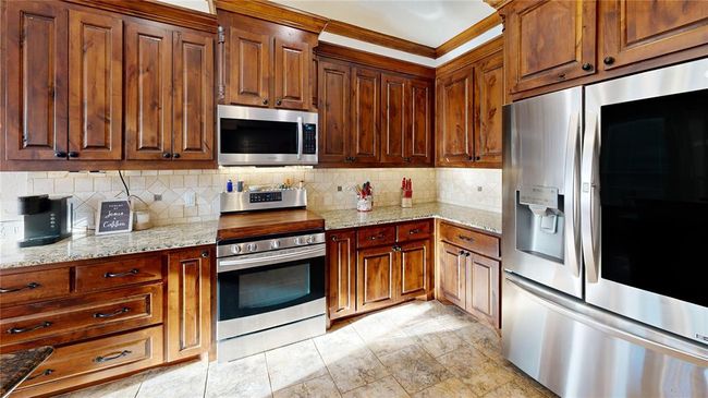 Kitchen featuring decorative backsplash, light stone counters, brown cabinets, and appliances with stainless steel finishes | Image 23