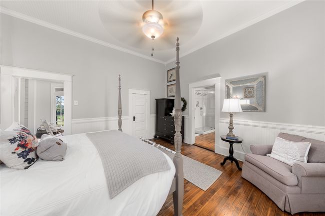 Bedroom featuring wainscoting, dark wood-style flooring, crown molding, ceiling fan, and ensuite bathroom | Image 17