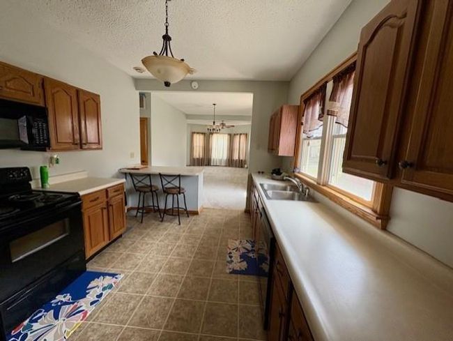 Kitchen featuring a textured ceiling, light countertops, tile patterned floors, pendant lighting, and black appliances | Image 16
