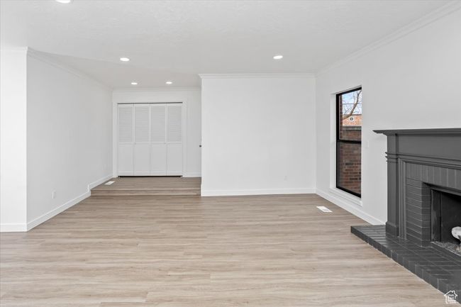 Unfurnished living room with baseboards, a fireplace, crown molding, and light wood-type flooring | Image 15
