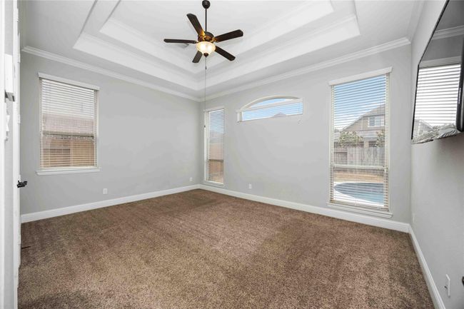 This generously sized room with neutral color palette, plush carpeting, and an elegant tray ceiling with a ceiling fan. Expansive windows flood the space with natural light while offering serene views of the pool area, creating a bright and welcoming ambiance. | Image 20