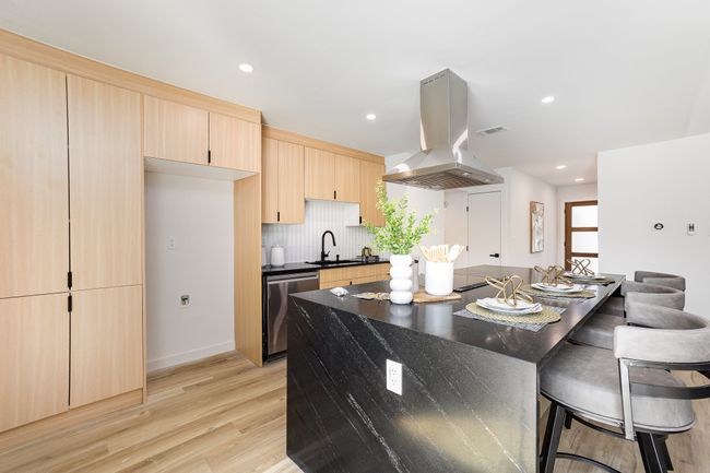 Kitchen featuring light wood-style flooring, a kitchen bar, dishwasher, island range hood, and light brown cabinets | Image 20