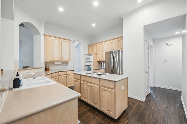 Kitchen featuring light brown cabinetry, white appliances, arched walkways, a kitchen island, and ornamental molding | Image 11