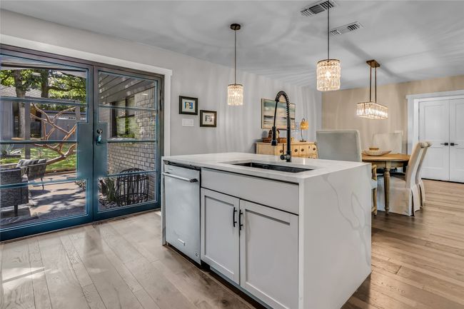Kitchen with a chandelier, wood-type flooring, stainless steel dishwasher, and decorative light fixtures | Image 13