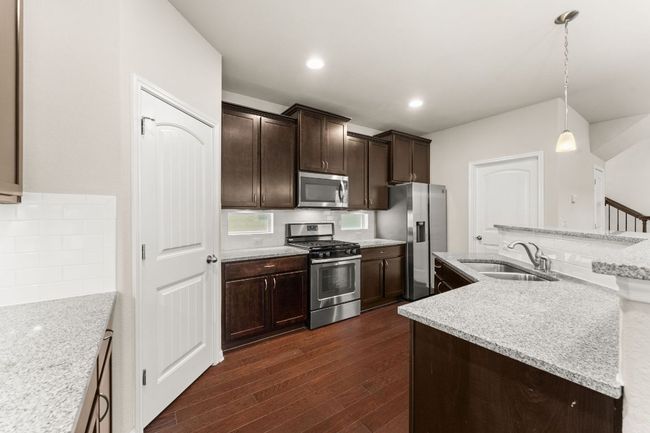 Kitchen with stainless steel appliances, a sink, dark wood finished floors, dark brown cabinetry, and decorative light fixtures | Image 6
