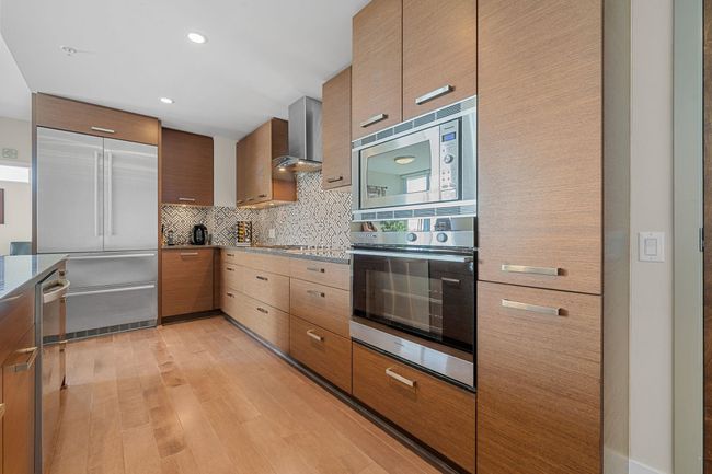 Kitchen with built in appliances, wall chimney exhaust hood, backsplash, light wood-style floors, and modern cabinets | Image 14