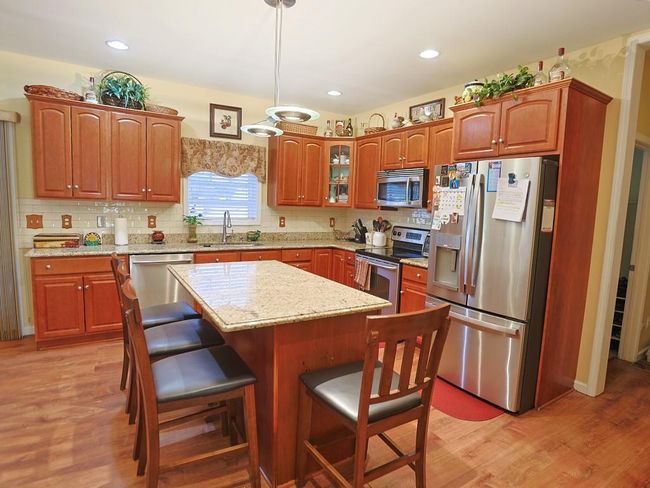 Kitchen with light wood-style flooring, a sink, a kitchen breakfast bar, and appliances with stainless steel finishes | Image 8