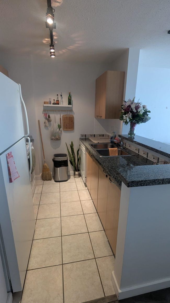 Kitchen with a sink, light tile patterned floors, dark countertops, dishwasher, and freestanding refrigerator | Image 8