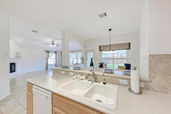 Kitchen featuring ceiling fan with notable chandelier, visible vents, a sink, white dishwasher, and open floor plan | Image 19