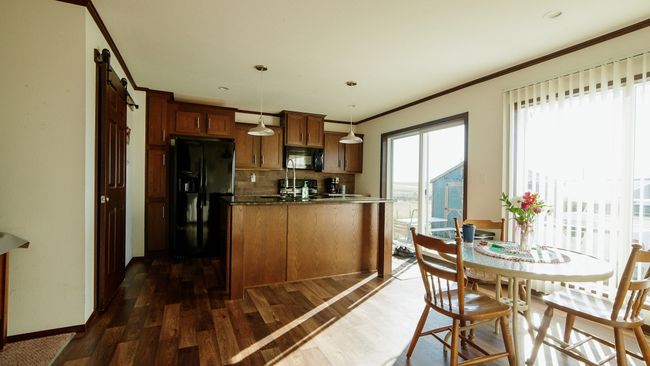 Kitchen featuring dark wood-style floors, brown cabinetry, ornamental molding, black appliances, and decorative light fixtures | Image 31