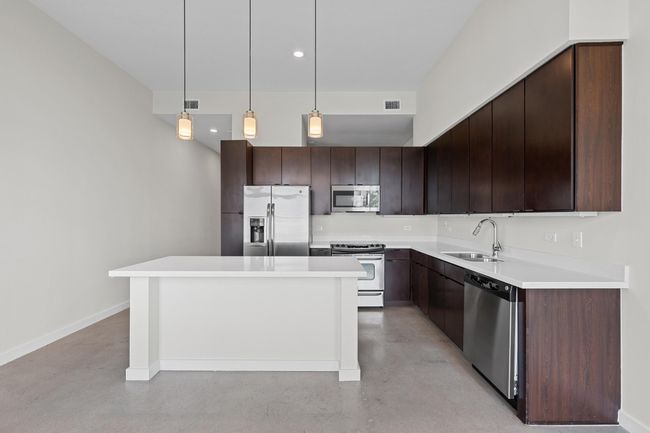 Kitchen featuring dark brown cabinetry, appliances with stainless steel finishes, a center island, a sink, and concrete floors | Image 7