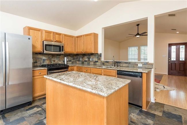 Kitchen with stainless steel appliances, lofted ceiling, ceiling fan, a center island, and decorative backsplash | Image 11