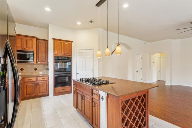 Kitchen featuring black appliances, arched walkways, brown cabinets, stone counters, and tasteful backsplash | Image 17
