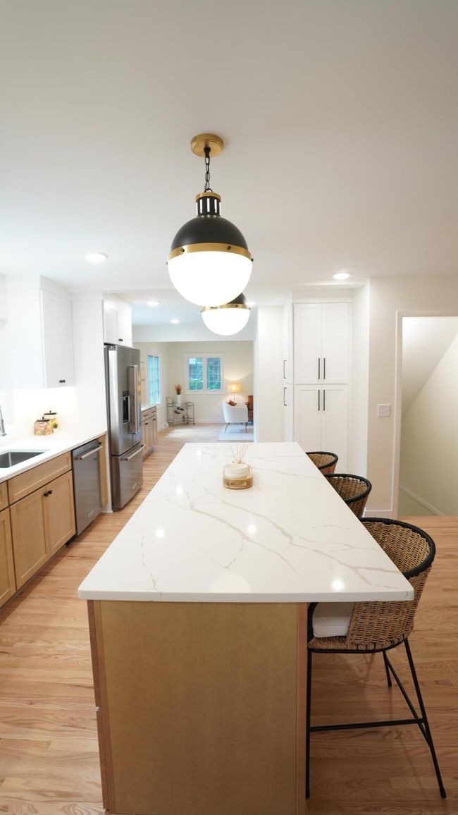 The eight foot kitchen island with quartz countertops is visually anchored by designer pendant lights and offers a KitchenAid built-in microwave and stained wood cabinetry with soft-close drawers. | Image 26