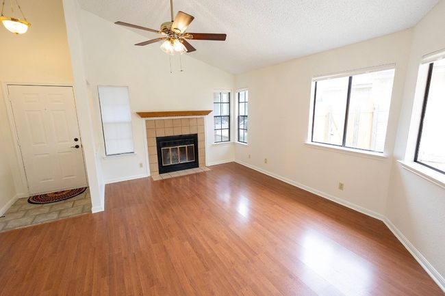 Unfurnished living room featuring ceiling fan, wood finished floors, a tiled fireplace, vaulted ceiling, and baseboards | Image 9