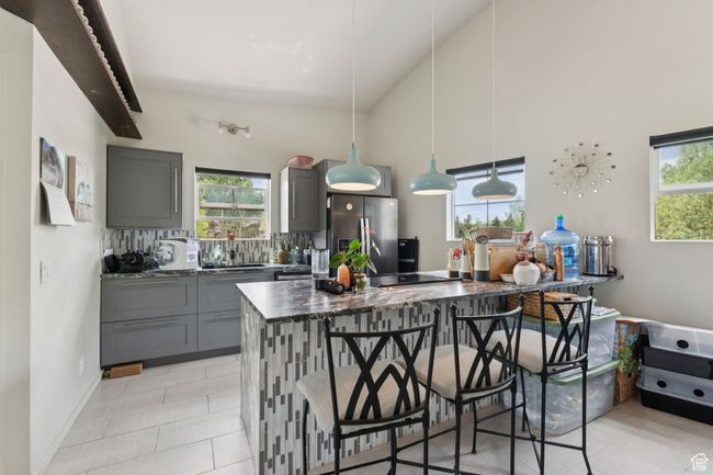 Kitchen featuring stainless steel refrigerator with ice dispenser, gray cabinetry, healthy amount of natural light, and high vaulted ceiling | Image 33