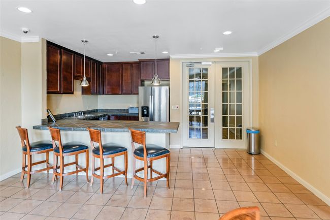 Kitchen with stainless steel fridge, a peninsula, a kitchen bar, dark countertops, and crown molding | Image 32