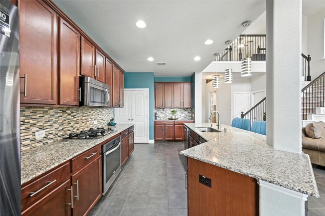Kitchen with decorative backsplash, light stone countertops, stainless steel appliances, an island with sink, and recessed lighting | Image 11