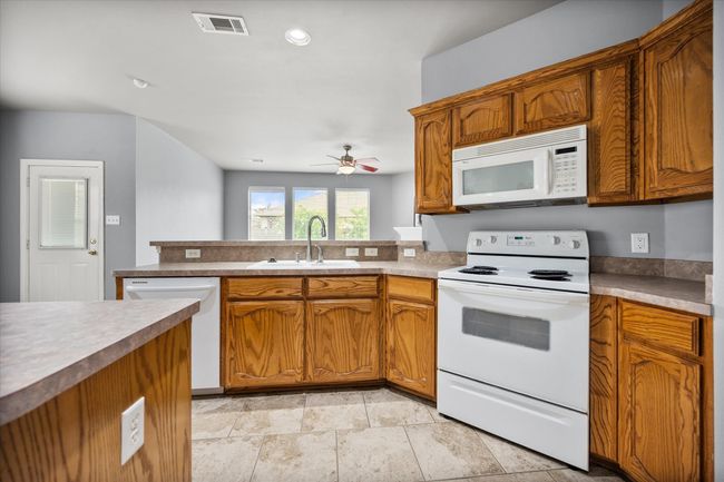 Kitchen with white appliances, ceiling fan, brown cabinets, a peninsula, and recessed lighting | Image 4