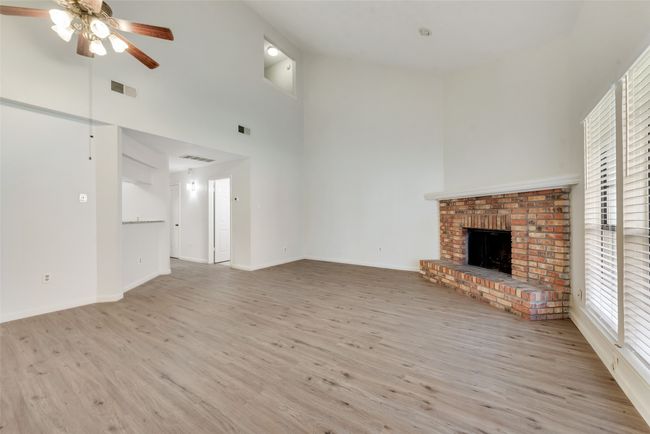 Unfurnished living room with wood finished floors, a fireplace, healthy amount of natural light, a ceiling fan, and a towering ceiling | Image 8