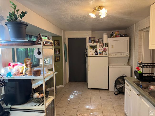 Kitchen with stacked washer / drying machine, white cabinets, light tile patterned floors, freestanding refrigerator, and a textured ceiling | Image 21