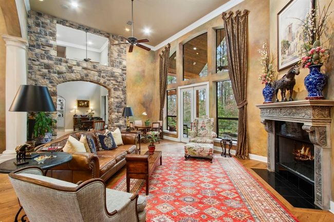 The French doors and wall of windows afford stunning views and provide effortless access to the covered veranda, patio and summer kitchen, overlooking the private and secluded acreage. The cast-stone mantle and granite hearth beautifully surround the crackling fireplace, enhancing the warm and intimate feeling of this spacious room. | Image 10
