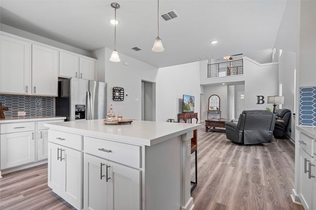 Kitchen with stainless steel refrigerator with ice dispenser, light wood finished floors, a kitchen island, light countertops, and backsplash | Image 15