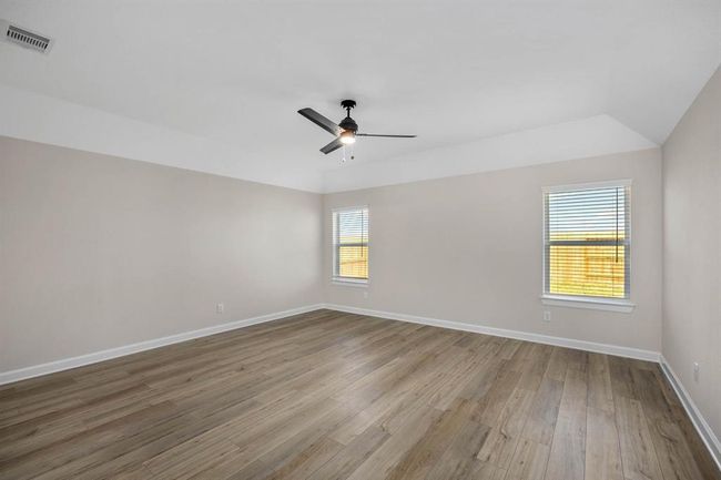 Step into luxury in the primary bedroom, where vinyl plank flooring and a ceiling fan combine to create a haven of comfort and style. Sunlight streams through the windows, bathing the space in natural light and offering views of the tranquil surroundings. A doorway leads to the en-suite bathroom, providing a private sanctuary for relaxation and self-indulgence. | Image 5