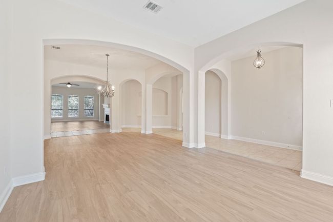 Empty room with arched walkways, ceiling fan with notable chandelier, baseboards, visible vents, and light wood-style floors | Image 14