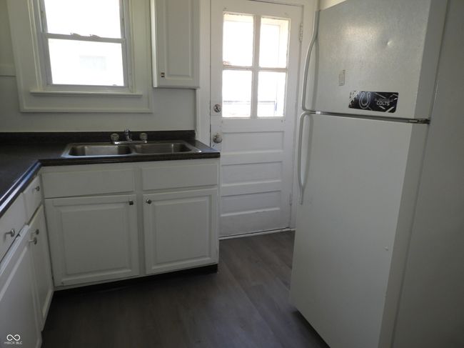 kitchen with a sink, freestanding refrigerator, white cabinetry, dark countertops, and dark wood-type flooring | Image 7
