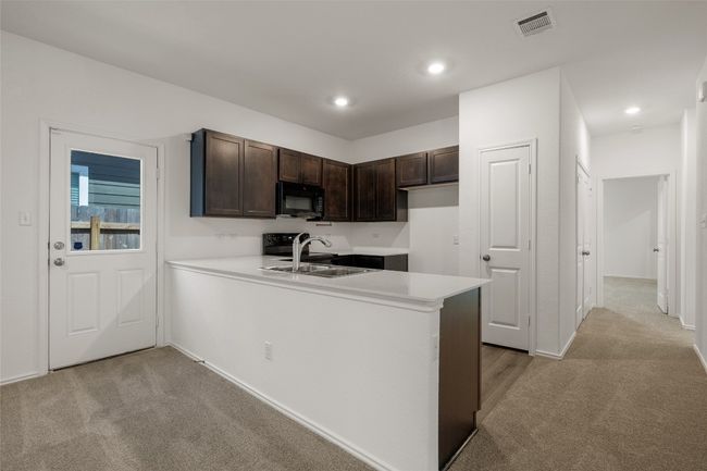 Kitchen featuring black microwave, light colored carpet, dark brown cabinets, a peninsula, and recessed lighting | Image 17