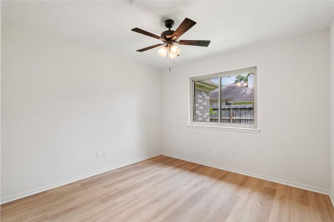 Third bedroom with ceiling fan, wood-like flooring, and a clear layout for multiple uses. | Image 22