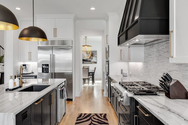 Kitchen with custom exhaust hood, white cabinets, light wood-style floors, dark cabinetry, and decorative backsplash | Image 14