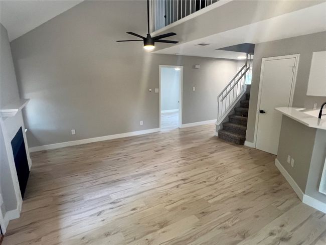 Unfurnished living room featuring ceiling fan, light wood-type flooring, high vaulted ceiling, stairway, and a fireplace | Image 8
