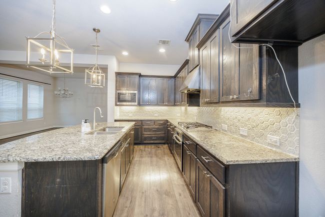 Kitchen featuring stainless steel appliances, a chandelier, light wood finished floors, under cabinet range hood, and decorative backsplash | Image 20