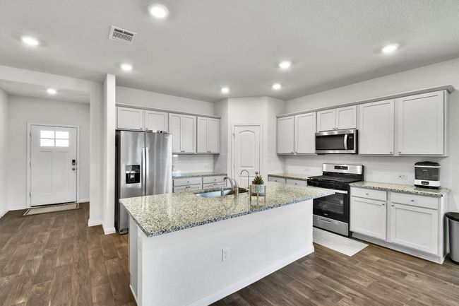 Kitchen with appliances with stainless steel finishes, a sink, dark wood-style floors, an island with sink, and light stone countertops | Image 8