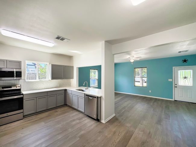 Kitchen with appliances with stainless steel finishes, gray cabinetry, decorative backsplash, and wood finished floors | Image 7