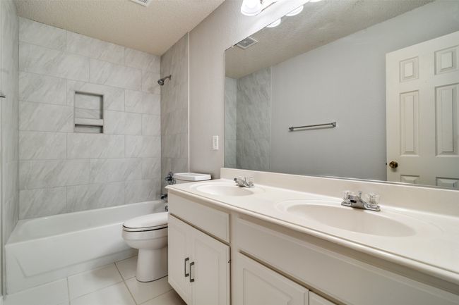 Bathroom with bathtub / shower combination, a textured ceiling, double vanity, and light tile patterned floors | Image 16