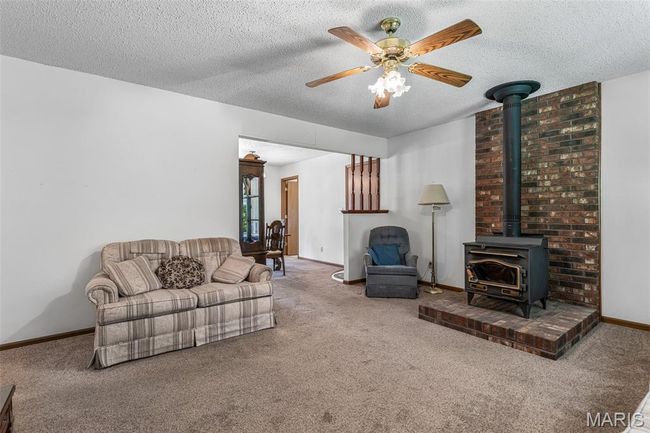Carpeted living area with a wood stove, ceiling fan, a textured ceiling, and baseboards | Image 11
