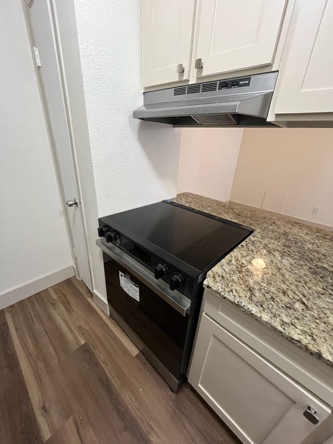 Kitchen with black range with electric stovetop, under cabinet range hood, dark wood-type flooring, and white cabinets | Image 5