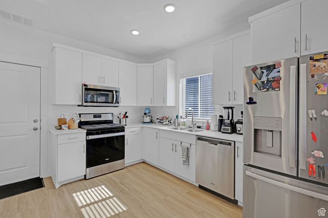 Kitchen with appliances with stainless steel finishes, a sink, light wood-style floors, light countertops, and white cabinetry | Image 8