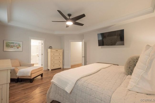 Bedroom featuring a tray ceiling, wood finished floors, connected bathroom, and ceiling fan | Image 16
