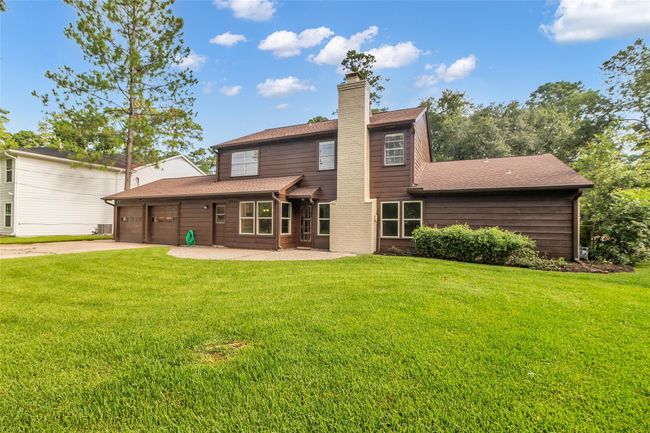 This photo showcases a charming two-story home with a dark exterior and a spacious two-car garage. It's surrounded by a lush, well-maintained lawn and framed by mature trees, offering a serene and inviting atmosphere. | Image 37